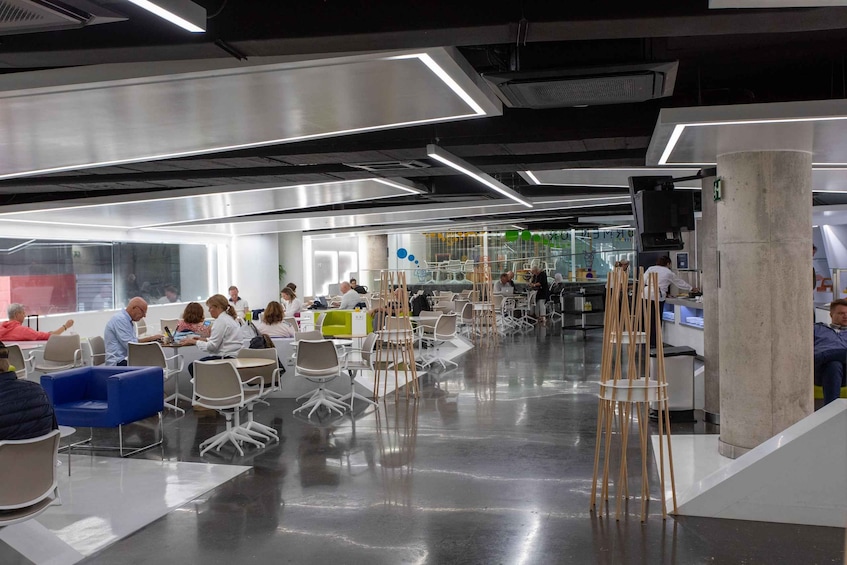 Un espace de bureau moderne où l’on voit des personnes travaillant à des bureaux, un mur en verre et un pilier en béton. 2