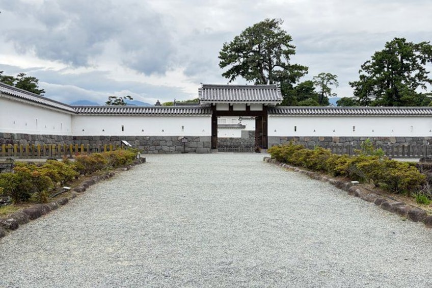 A traditional Japanese gate with a gravel path leading up to it, surrounded by stone walls and greenery. 5
