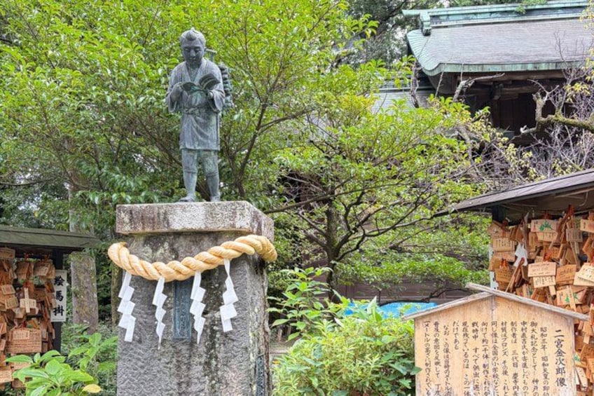 A statue on a pedestal with a rope and paper tags, surrounded by greenery and traditional buildings. 4