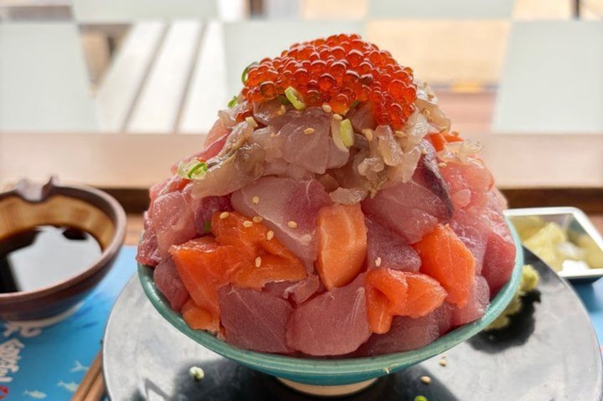 A bowl of sashimi with salmon, tuna, and other fish, topped with salmon roe and garnished with green onions and sesame seeds. 1