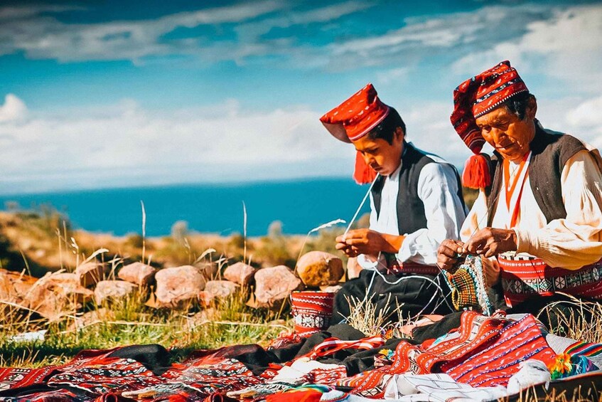 Two individuals engaged in textile weaving, surrounded by colorful fabrics and traditional attire, with a mountainous landscape and a clear sky in the background. 3