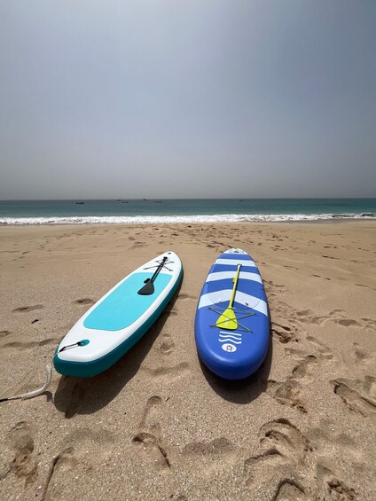 Two paddleboards on a sandy beach with footprints, and the ocean in the background. 1