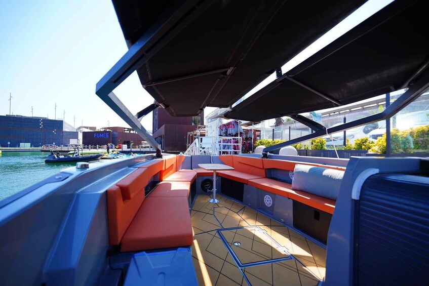 Cubierta de barco con asientos naranja, una pequeña mesa y vistas al agua y edificios al fondo. 4