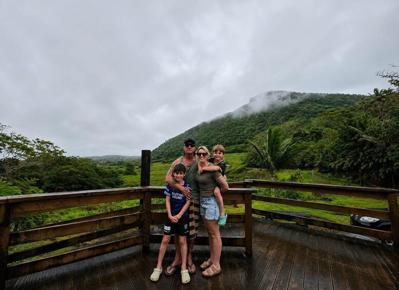 Una famiglia su un pontile di legno con vista su un paesaggio verdeggiante e una montagna sullo sfondo. 4