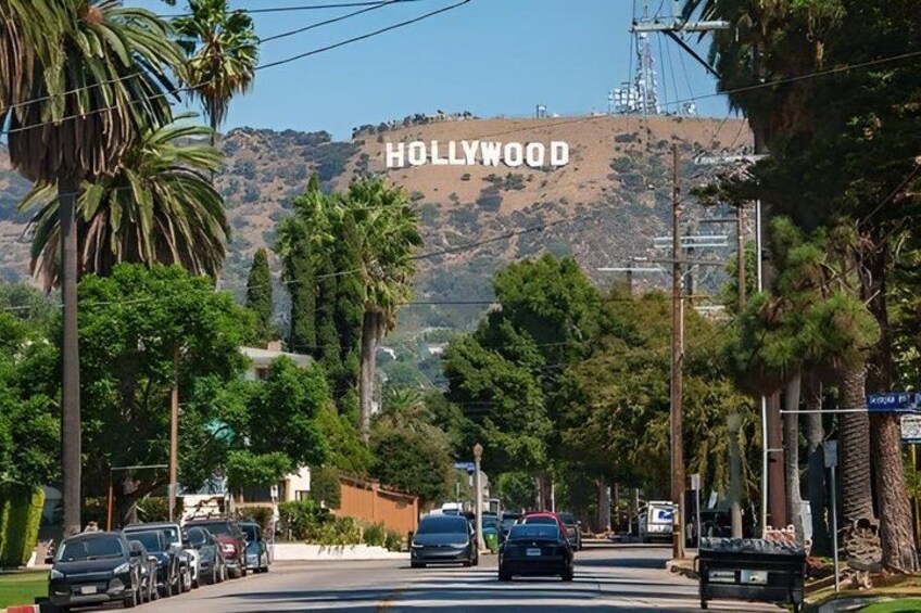 A street with cars, palm trees, and the Hollywood sign in the background. 1