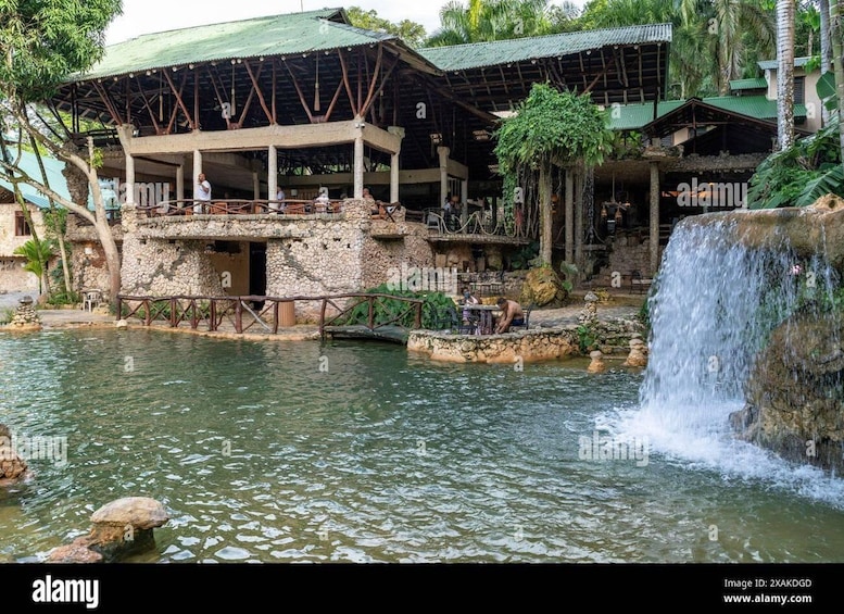 Ein rustikales Steinhaus mit einem grünen Dach, eine Holzbrücke über einem ruhigen Fluss und ein Wasserfall. 5