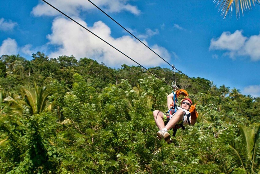 Eine Person saust mit einer Zipline durch einen dichten Wald, über ihr strahlt ein klarer Himmel. 1