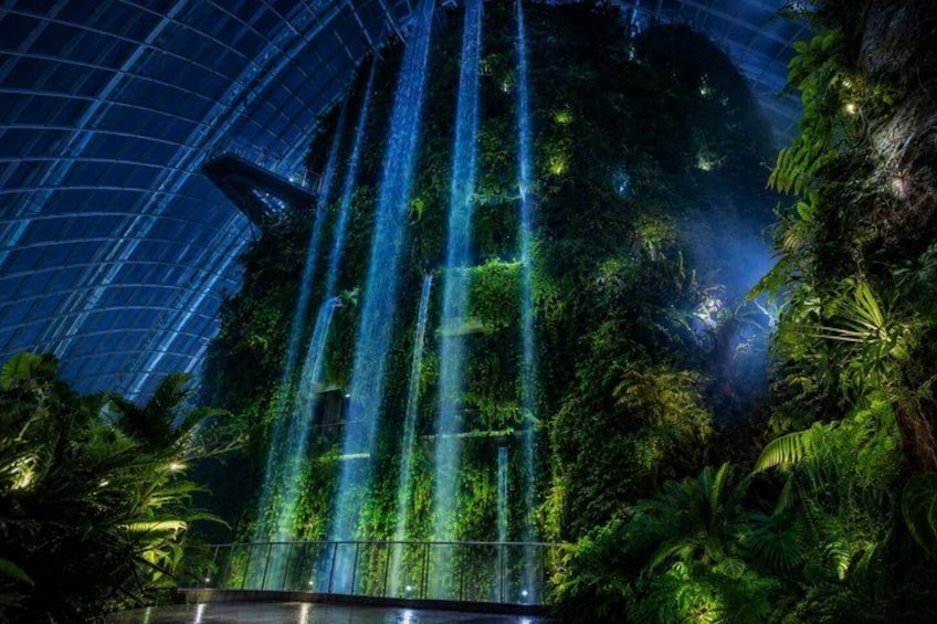 A large indoor waterfall, lush greenery, and a glass ceiling structure. 1