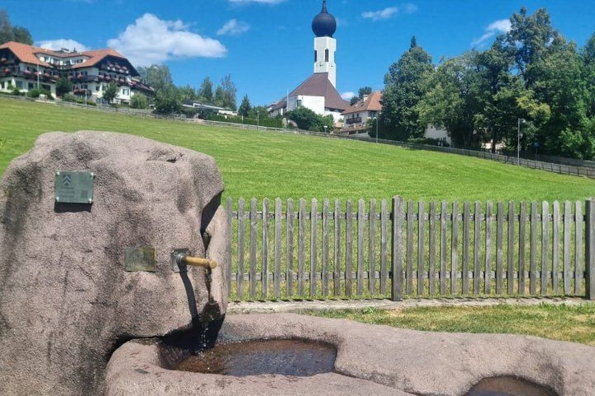 A stone fountain with a plaque, a wooden fence, and a church with a dome in the background. 3