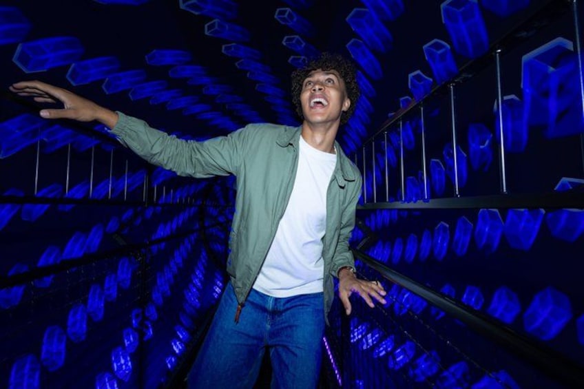 A person standing in a tunnel with blue lighting and geometric patterns on the walls. 2