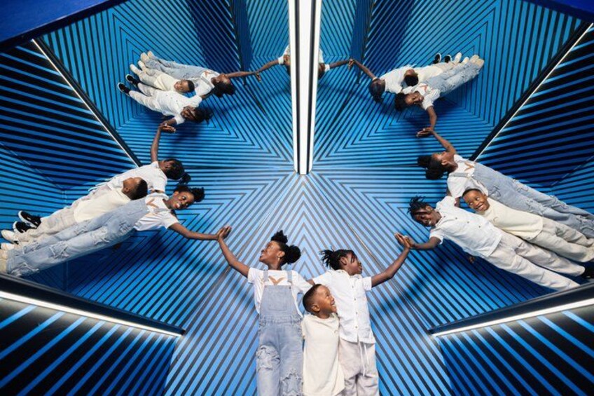 A group of children in white shirts and denim overalls, standing in a mirrored geometric pattern. 1