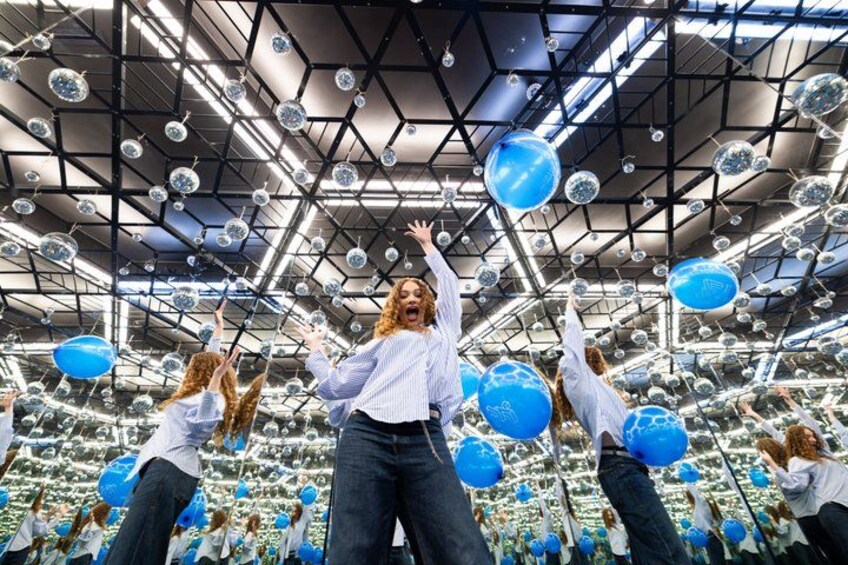 A person in a white shirt and jeans in a room with a geometric ceiling and blue spherical decorations. 4