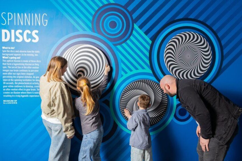 A family interacting with spinning discs on a blue patterned wall. 3