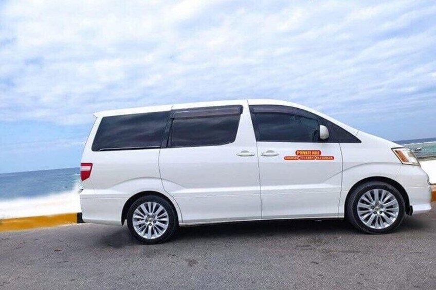 A white van parked on a road with a coastal background. 3