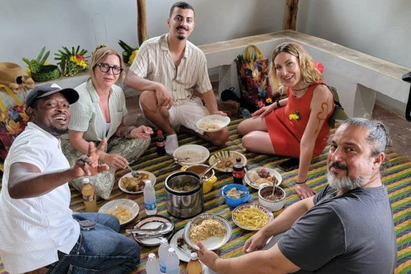 A group of people sitting on a striped mat, eating various dishes. 1