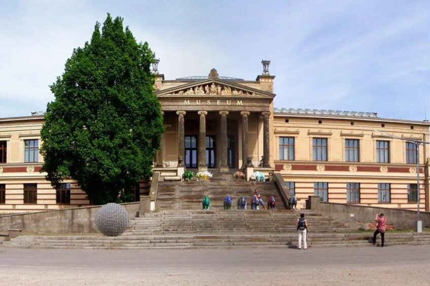 A museum with classical architecture, a large tree, and people walking on the steps. 4
