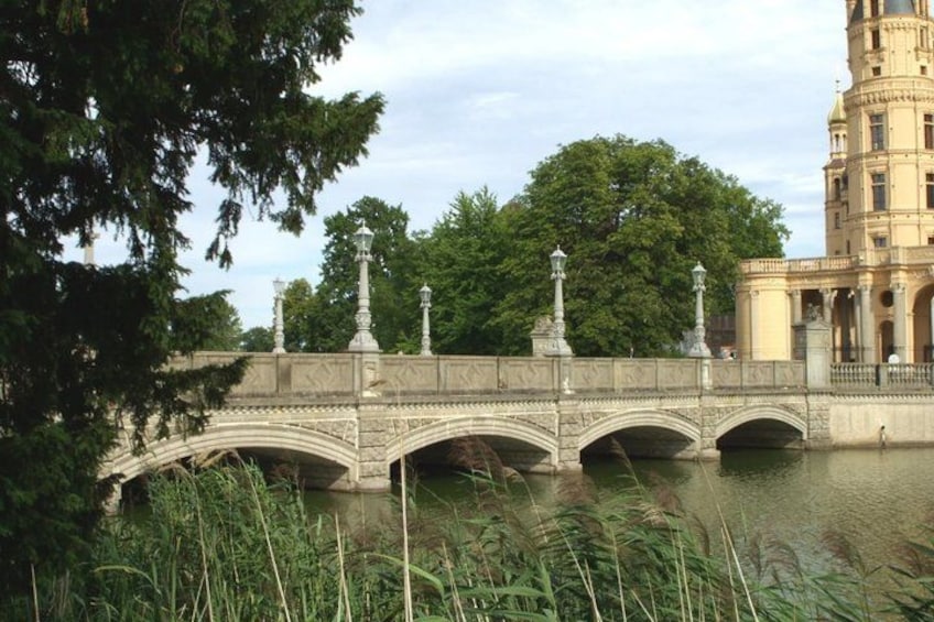 A stone bridge over a body of water, surrounded by trees and a large building with a tower. 3