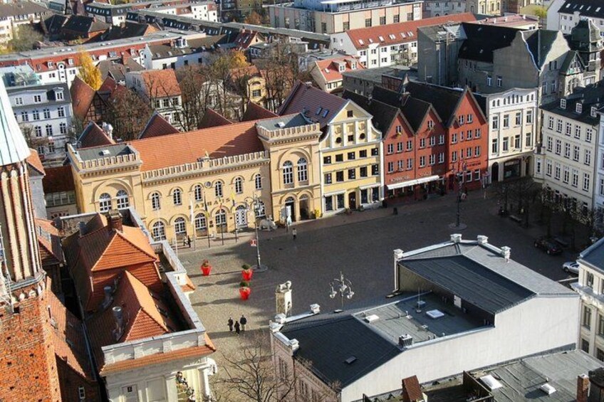 A European town square with historic buildings, a central open space, and a few pedestrians. 5
