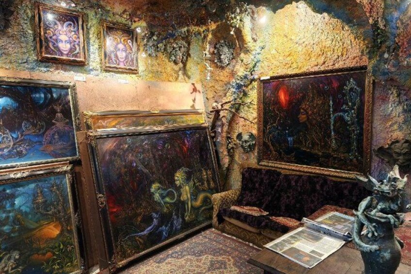 A room with eclectic art, including a large painting of a figure with a red halo, a statue, and various framed artworks on the walls. 2