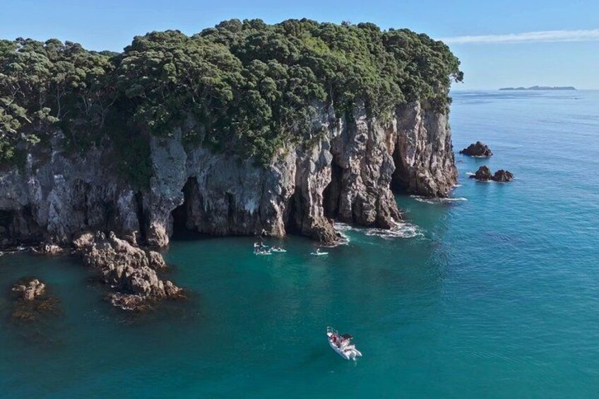 A coastal landscape with a rocky cliff, clear turquoise waters, and a person paddling a kayak. 4