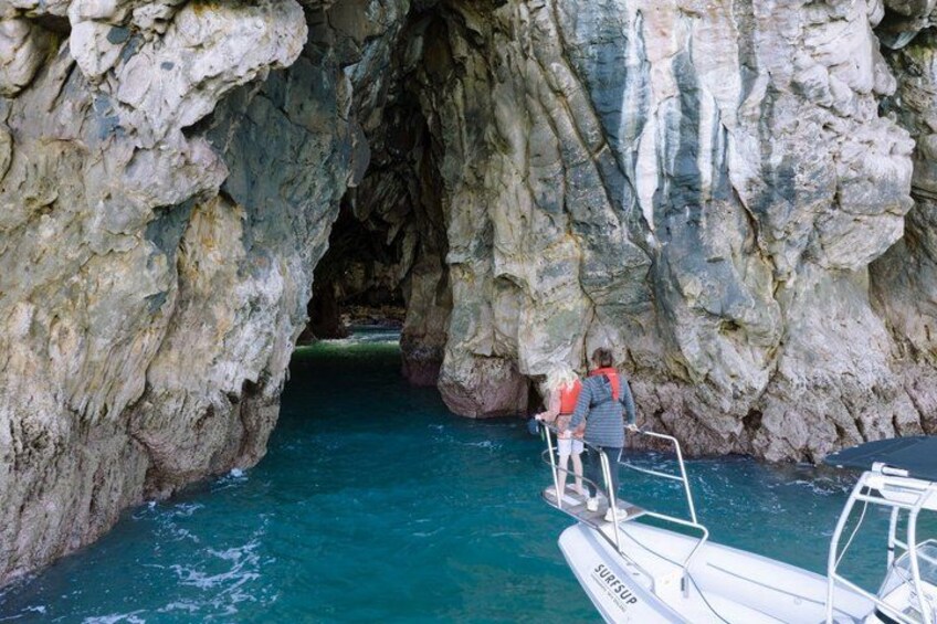 A cave entrance with water flowing through it, a boat with people on it, and rocky cliffs. 5