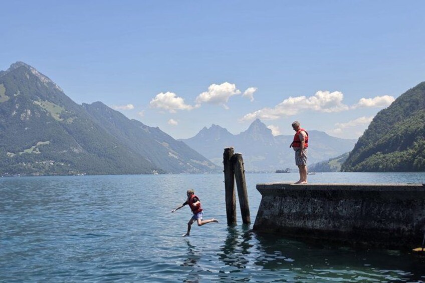 A lake with mountains in the background, a dock, and a person jumping into the water. 1