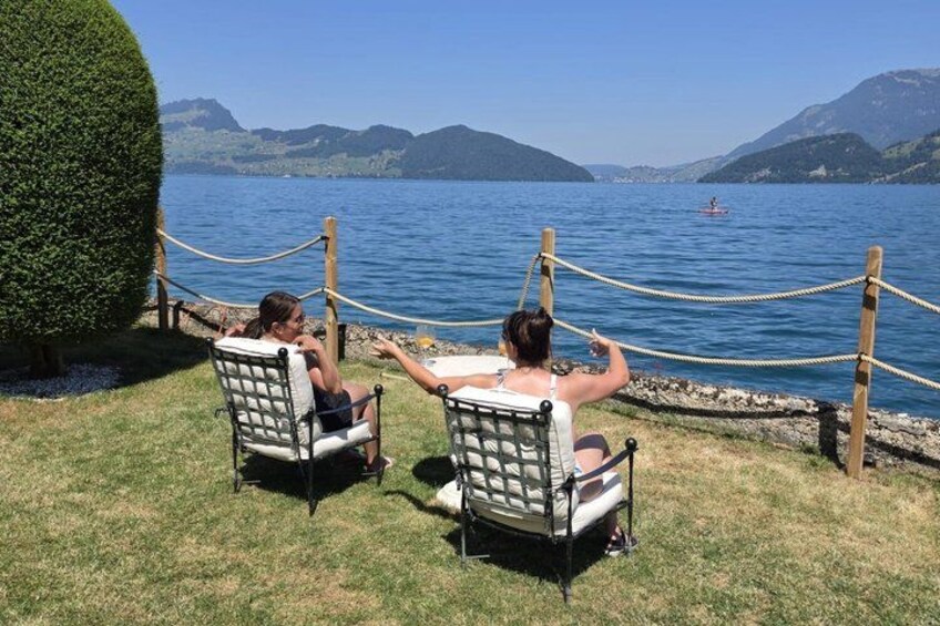 Two people relaxing on chairs facing a lake with mountains in the background. 3