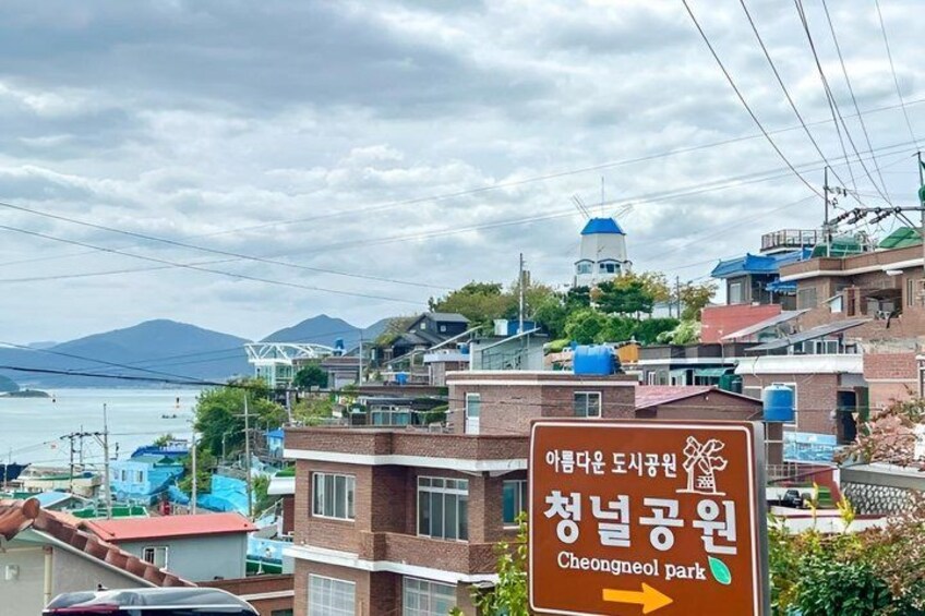A sign for Cheongneol Park with a view of a coastal town and mountains in the background. 5