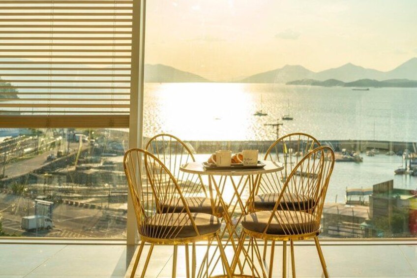 A table with chairs by a window overlooking a marina with boats and distant mountains. 3