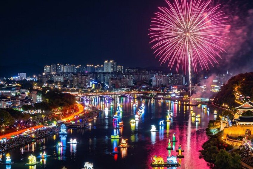 A cityscape at night with a river reflecting lights, a bridge, and fireworks in the sky. 1