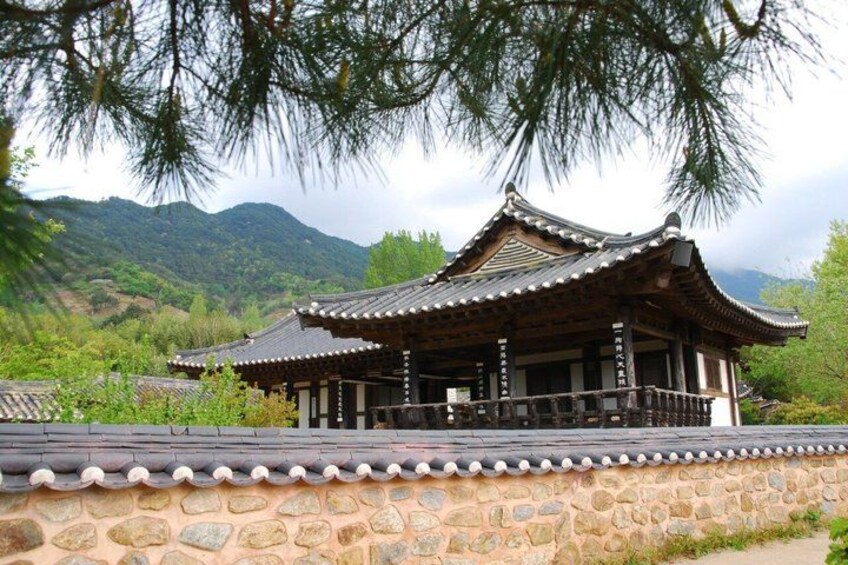 A traditional wooden building with a tiled roof, surrounded by stone walls and lush greenery. 2
