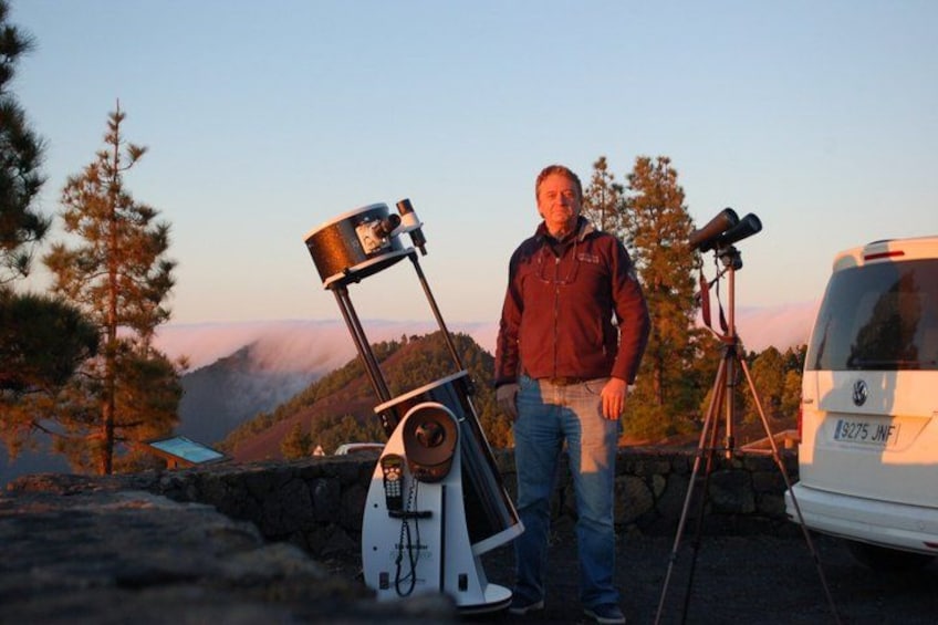 A person standing next to a telescope and a van in a mountainous area. 1