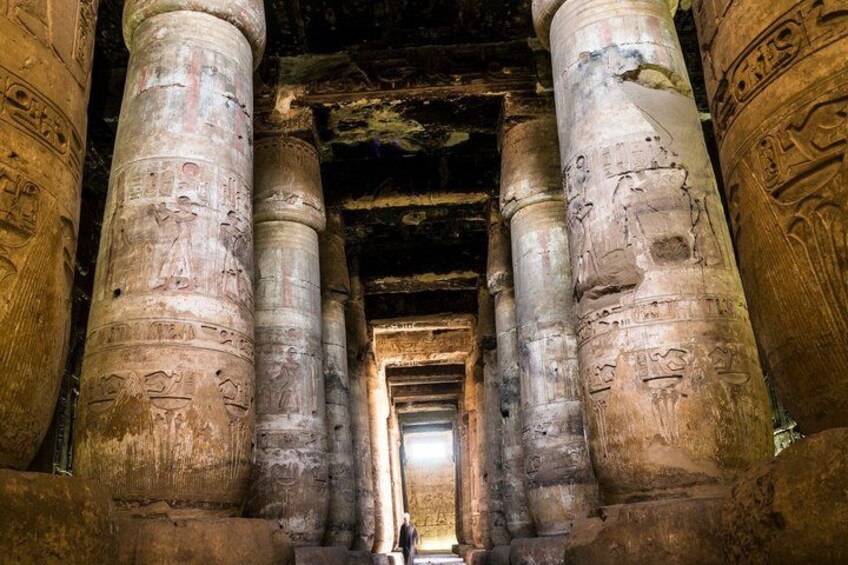 Ancient Egyptian columns with hieroglyphs, a person standing in the center, and a doorway leading to a dark interior. 5