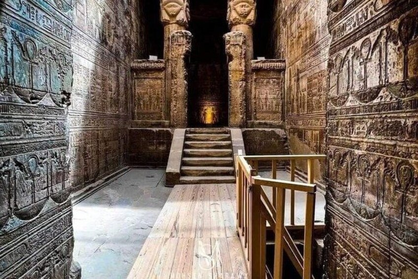 A corridor with hieroglyphic carvings, a wooden staircase, and a central column. 3