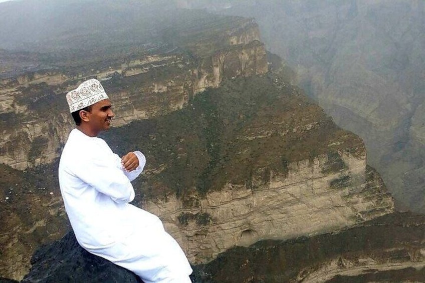 A person in traditional attire sitting on a cliff overlooking a canyon. 4