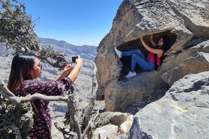 A person taking a photo of another person sitting in a rock crevice. 1