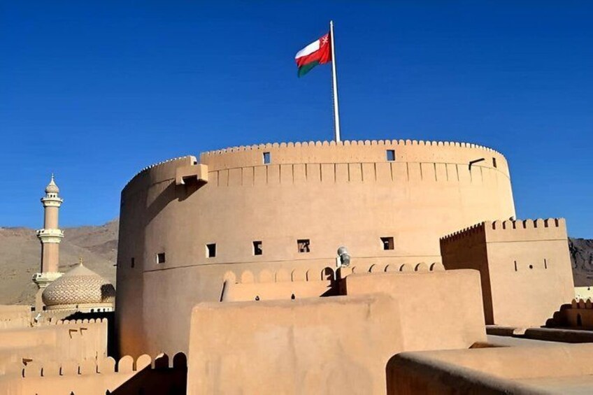 A large, circular fortress-like structure with a flag on top, a minaret, and a clear blue sky. 2