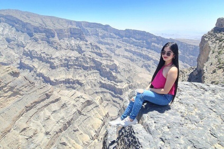 A person sitting on a rocky outcrop overlooking a vast canyon with layered rock formations. 4