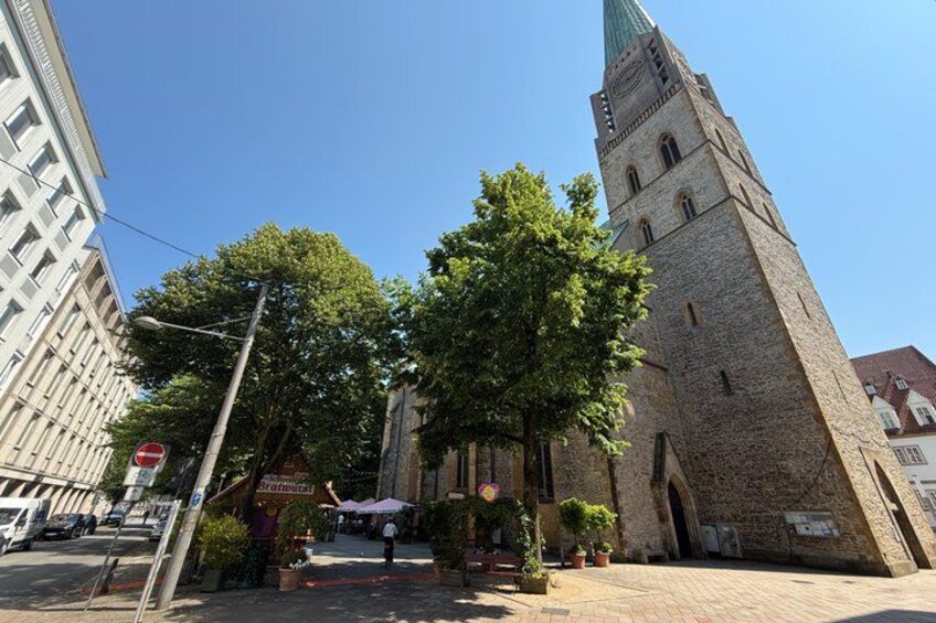 A historic church with a tall tower, a street with cars, and a clear blue sky. 5