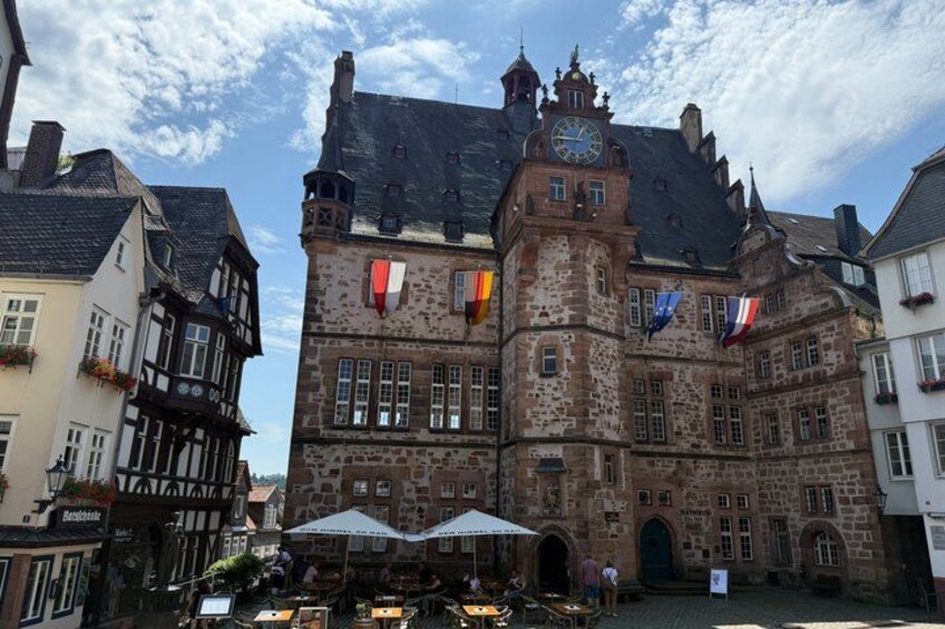 A historic building with a clock tower, flags, and a cobblestone street. 5