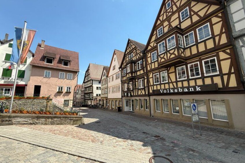 A cobblestone street lined with traditional half-timbered houses, a Volksbank building, and a clear blue sky. 4