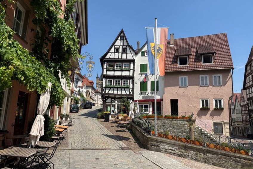 A cobblestone street lined with traditional half-timbered houses, a flagpole with flags, and outdoor seating. 5