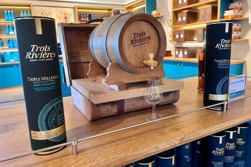 A wooden barrel with a tap, a glass, and bottles of Trois Rivières wine on a shelf. 3