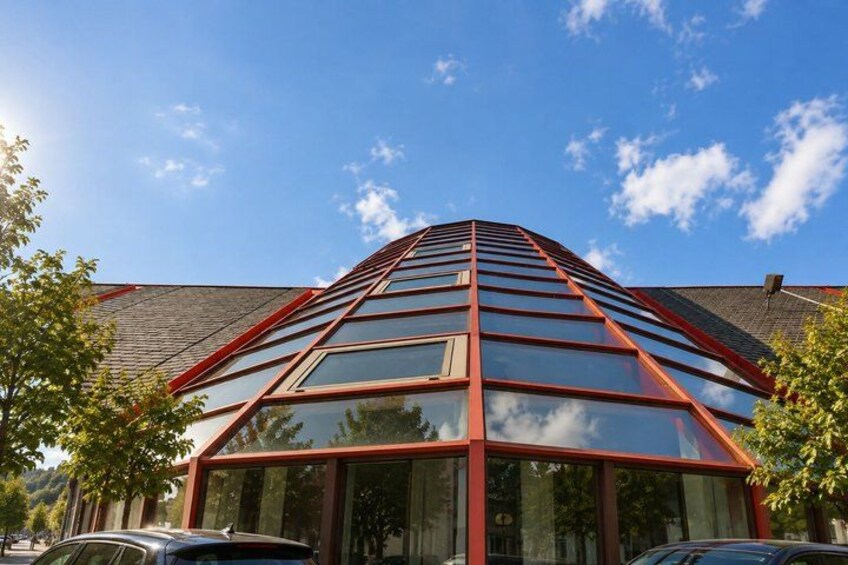A modern building with a glass facade and red framing, surrounded by trees and parked cars. 5