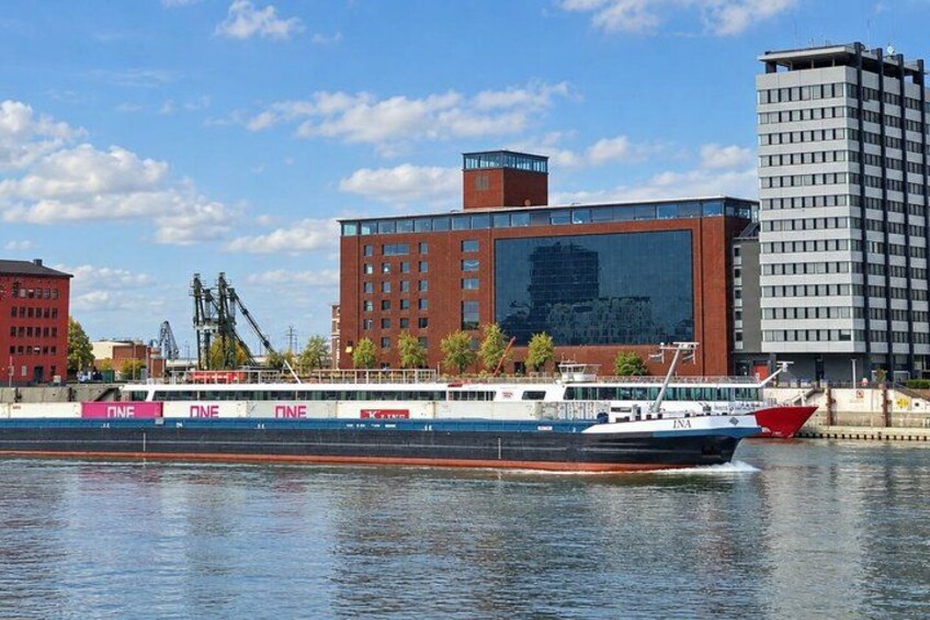 A river with a ferry, buildings, and cranes in the background. 3