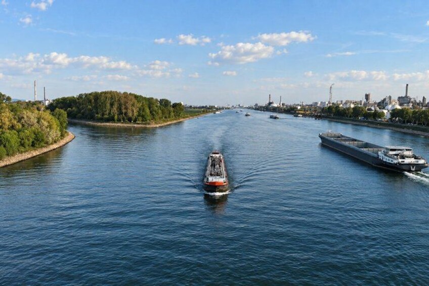 A river with a boat in the center, a larger ship on the right, and industrial buildings in the background. 5
