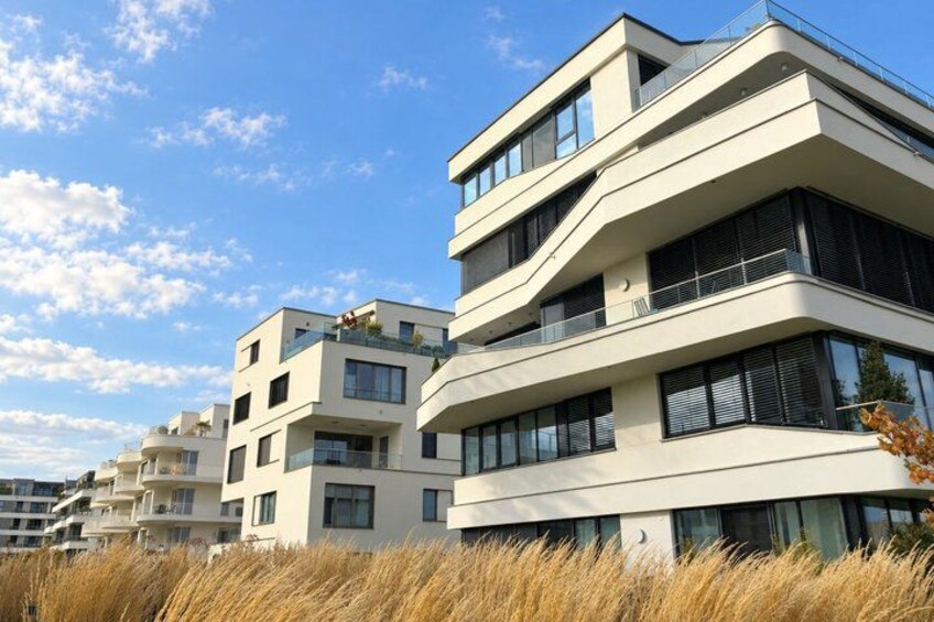 A modern multi-story residential building with balconies, surrounded by tall grass. 4