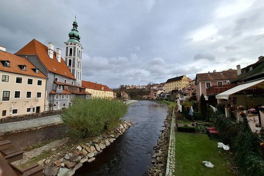 A river with buildings on both sides, a church with a green spire, and a grassy area with flowers. 4