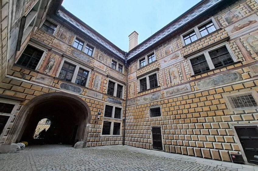 A courtyard with a brick wall, an archway, and a cobblestone ground. 3