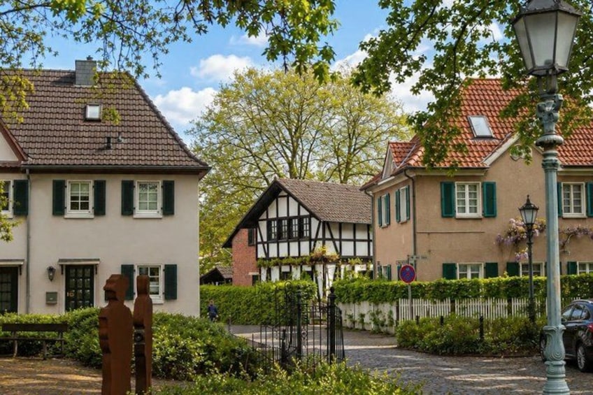 A quaint European village with traditional half-timbered houses, a cobblestone street, and a statue of a man. 4